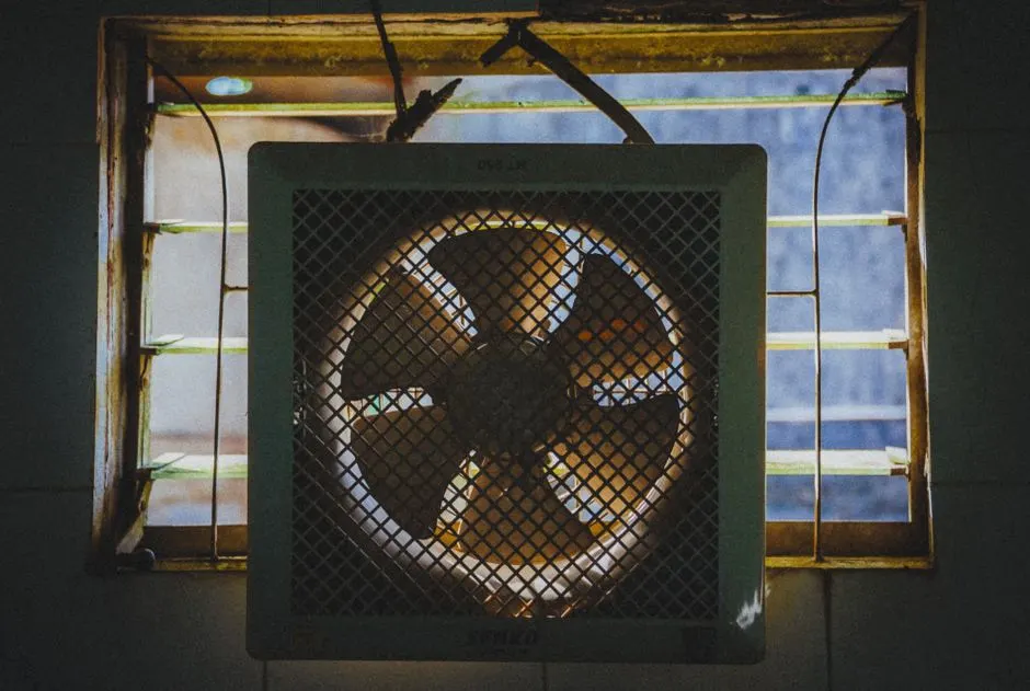 A vintage exhaust fan installed in a rustic window frame, casting dramatic shadows.
